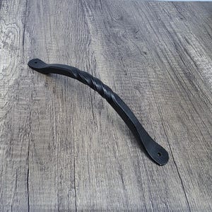 May include: Black metal door handle with a twisted design. The handle is about 8 inches long and has a rounded end.