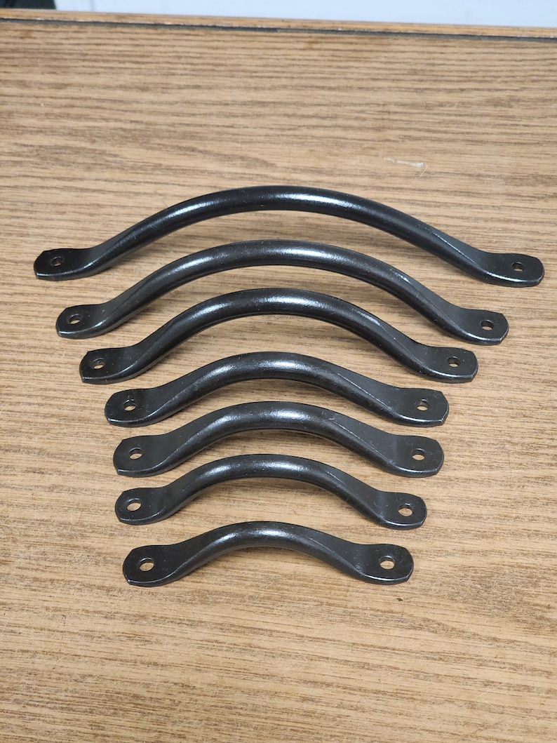 Puede incluir: Conjunto de seis tiradores de metal negro con un dise&ntilde;o curvo. Los tiradores est&aacute;n dispuestos en fila, con el tirador m&aacute;s grande en la parte superior y el m&aacute;s peque&ntilde;o en la parte inferior.