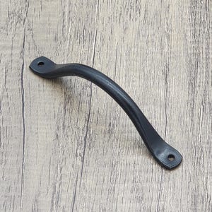 May include: Black metal door handle with a curved design. The handle is approximately 6 inches long.