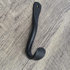 May include: Black metal hook with a curved design. The hook is mounted on a wooden surface.