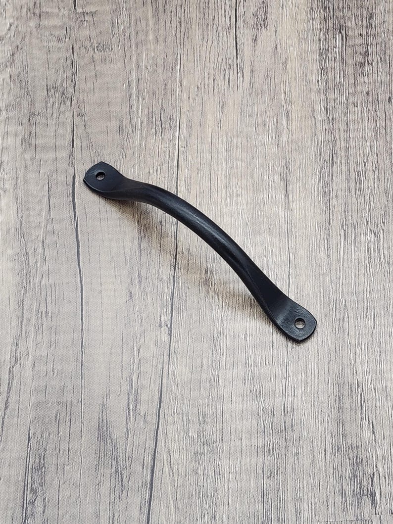 Puede incluir: Tirador de armario de metal negro con dise&ntilde;o curvo. El tirador tiene dos agujeros para montaje.