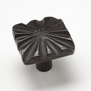 May include: A dark bronze square cabinet knob with a textured, sunburst design. The knob has a decorative, wavy edge and a cylindrical stem. This hardware is suitable for drawers and cabinets.