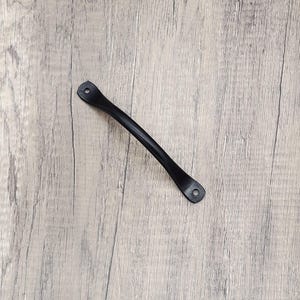 Puede incluir: Tirador de caj&oacute;n de metal negro con bordes redondeados y dos agujeros para tornillos.