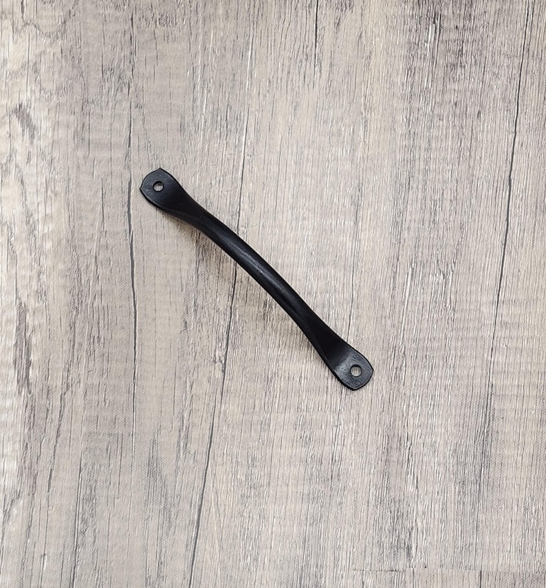 Puede incluir: Tirador de caj&oacute;n de metal negro con bordes redondeados y dos agujeros para tornillos.