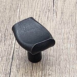 May include: Black metal cabinet knob with a rounded, slightly curved shape. The knob has a smooth, matte finish.