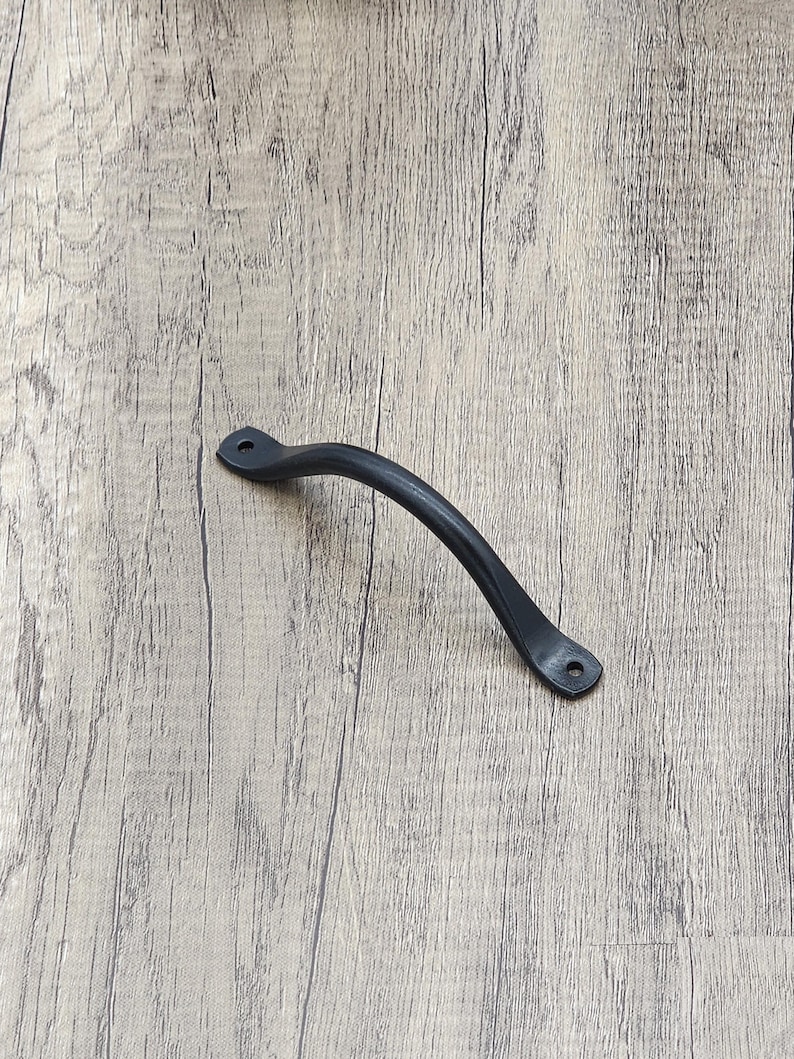 Puede incluir: Tirador de armario de metal negro con dise&ntilde;o curvo. El tirador tiene dos peque&ntilde;os agujeros para el montaje.