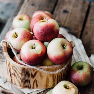 May include: A wooden bowl filled with red and green apples. The apples are arranged in a pile, with some spilling out of the bowl. The bowl is sitting on a wooden table.