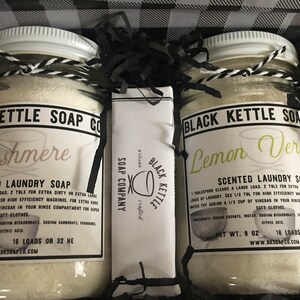 May include: Two glass jars of laundry soap, one labeled "Cashmere" and the other "Lemon Verbena", with a bar of soap labeled "Black Kettle Soap Company" in the middle. Each jar contains 8 ounces of soap and makes 16 loads.