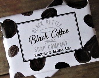 May include: White bar of soap with a black and white label that says "Black Kettle Black Coffee Soap Company Handcrafted Artisan Soap". The soap has a coffee bean pattern.