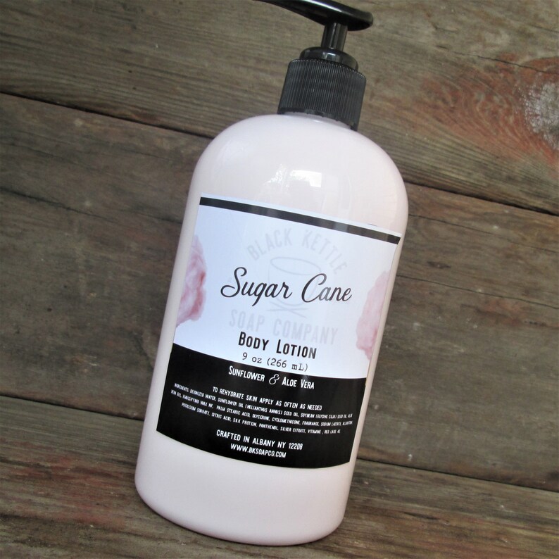 May include: A white pump bottle of Sugar Cane Body Lotion from Black Kettle Soap Company. The label features a pink cotton candy graphic and the text "Sugar Cane Body Lotion 9 oz (266 mL) Sunflower & Aloe Vera".