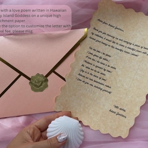 May include: A light pink envelope with gold trim and a gold wax seal featuring a heart, accompanied by a piece of parchment paper with scalloped edges containing a poem in Hawaiian and English, and a white seashell-shaped object.