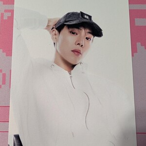 May include: A photograph of a person wearing a white zip-up hoodie and a dark gray baseball cap. The cap has a small, white rectangular patch with the letters "CG" on it. The person is looking at the camera.