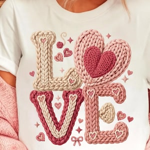 May include: White t-shirt featuring the word "LOVE" in a knitted design. The letters are in shades of pink and beige, with heart and star accents. The design has a 3D effect.