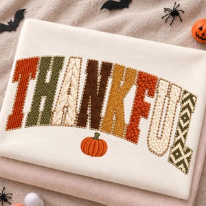 May include: A cream-colored sweatshirt featuring the word THANKFUL in large, block-style letters. Each letter displays a unique texture, including ribbed, herringbone, cable knit, suede, fuzzy, and geometric patterns, with a small orange pumpkin below.