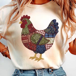 May include: Cream-coloured sweatshirt with a patchwork chicken design. The chicken is made up of various fabric patterns in red, green, blue, and white. The rooster's comb and beak are red and yellow.