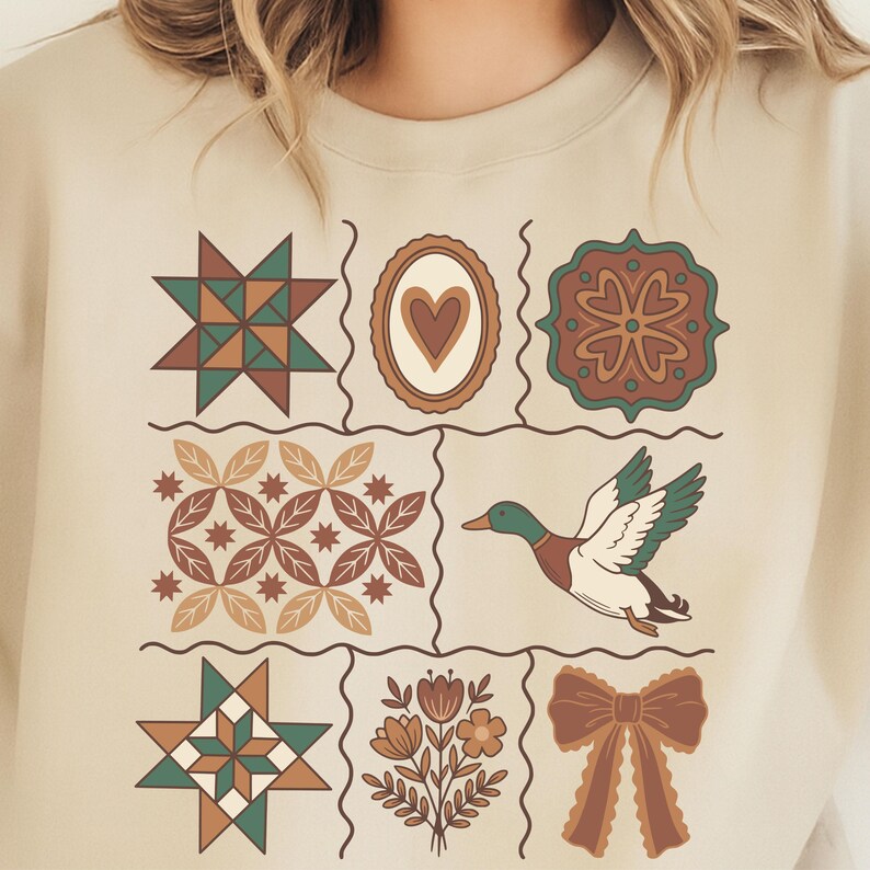 May include: Beige sweatshirt with a grid of decorative designs. The designs include a starburst, a heart, a floral pattern, a flying duck, and a bow. The colour palette includes shades of green, brown, and beige.