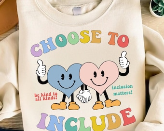 May include: Cream-colored sweatshirt with the words "CHOOSE TO INCLUDE" in colorful, retro-style lettering. Two smiling heart characters hold hands, with thumbs up. Text reads "be kind to all kinds!" and "inclusion matters!"