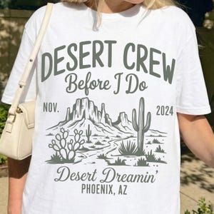 May include: White t-shirt with a desert-themed graphic. The design features the text "DESERT CREW Before I Do" above a desert landscape with cacti and mountains. Below the graphic, it reads "Desert Dreamin' PHOENIX, AZ" and "NOV. 2024".