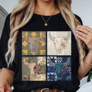 May include: Black t-shirt featuring a square design with four images of a bull skull decorated with flowers. The bull skulls are in different colors and patterns, including floral and geometric designs. The shirt is made of a soft material.