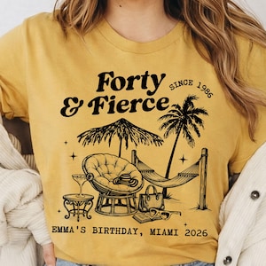 Può includere: T-shirt giallo senape con un design grafico nero. Il design include il testo "Forty & Fierce" con "Since 1986" sopra una scena tropicale con un'amaca, una palma e una sedia a sdraio. Il testo "Emma's Birthday, Miami 2026" è sotto.