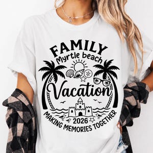 Può includere: T-shirt bianco con un design grafico nero. Il design include le parole "FAMILY Myrtle beach Vacation" con palme, conchiglie, un sole e un castello di sabbia. È incluso anche il testo "MAKING MEMORIES TOGETHER 2026".