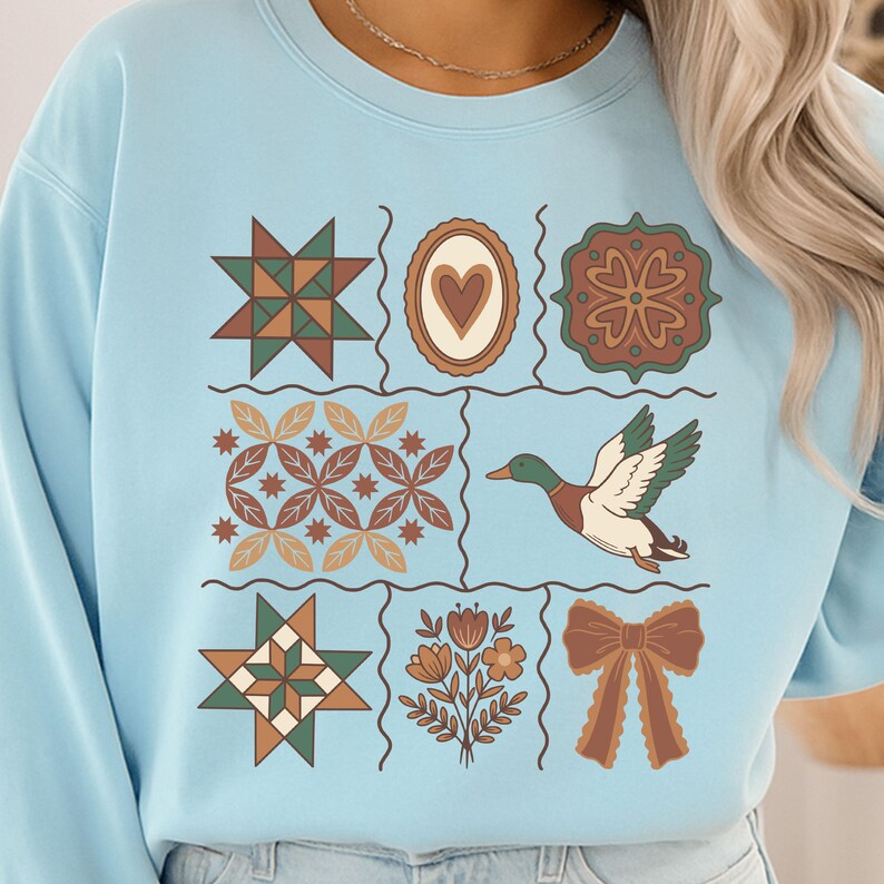 May include: Pale blue sweatshirt with a grid of decorative designs. The designs include a starburst, a heart, a floral pattern, a duck, and a bow. The sweatshirt is made of a soft material and is suitable for casual wear.