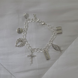 May include: A silver charm bracelet with religious themed charms, including a cross, a fish, a book, wings, and a pearl. The charms are attached to a silver chain.