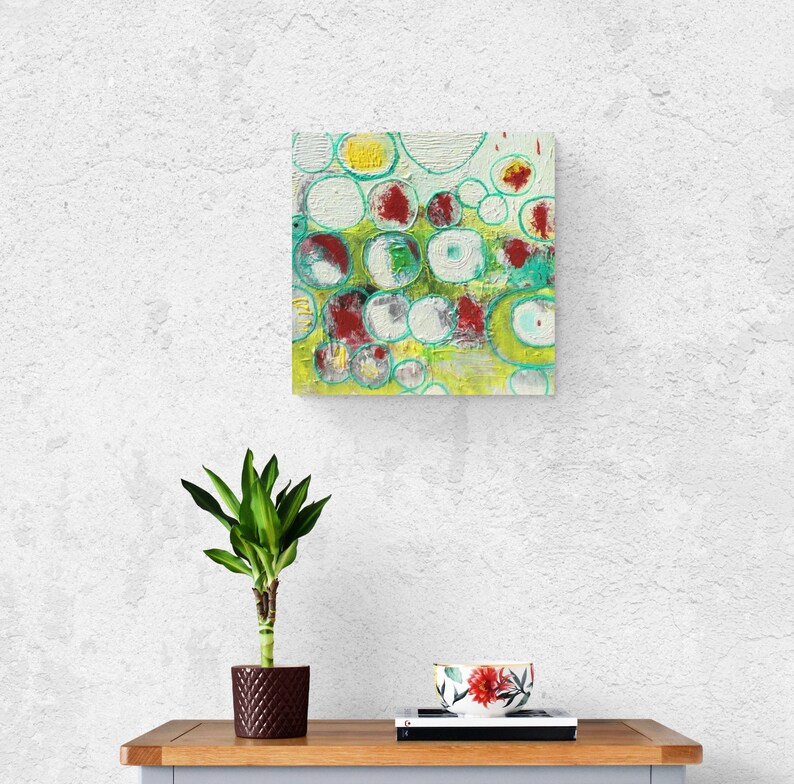 May include: Abstract painting with a green, yellow, white, and red color scheme. The painting features a pattern of overlapping circles with a textured surface.
