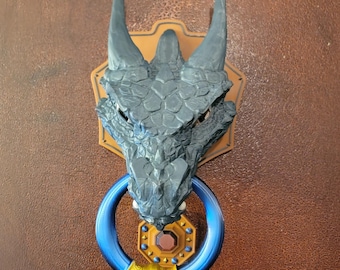 May include: A black dragon head door knocker with a blue and gold ring. The dragon has a textured, scaly surface and is mounted on a wooden door.
