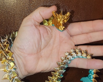 May include: A gold and turquoise necklace with a dragon head pendant. The necklace is made of small, interlocking pieces that resemble scales. The dragon head is detailed and has a fierce expression.