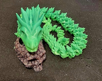 May include: A green articulated dragon figurine with a detailed head and spiky spine. The dragon's head is a lighter shade of green, and the base is a dark brown color. The dragon is posed on a dark surface.