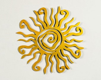 May include: A golden yellow sunburst wall decoration with a spiral centre and wavy rays is mounted on a white wall. A wooden table with a natural edge holds a vase with yellow calla lilies, a magazine, and two small, round, yellow decorative objects.