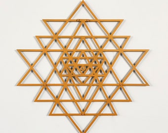 May include: A gold-colored metal sculpture of a Sri Yantra, a sacred geometric design from Hinduism. The sculpture is made of multiple overlapping triangles, creating a complex and intricate pattern.