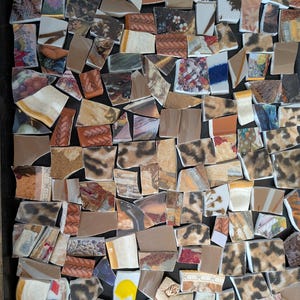 May include: A mosaic of broken ceramic pieces in various shapes and sizes. The fragments display a range of patterns, including floral designs, animal prints, and abstract art, with a color palette of browns, tans, and creams. The mosaic is set against a dark background.