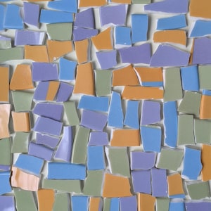 May include: A mosaic pattern composed of irregularly shaped ceramic tiles in shades of light blue, lavender, sage green, and muted orange. The tiles are arranged closely together with thin white grout lines separating each individual piece.