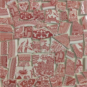 May include: A collection of broken ceramic pieces with red and white patterns. The fragments display various designs, including floral motifs, architectural scenes, and geometric shapes. The pieces are arranged closely together, creating a mosaic-like effect.
