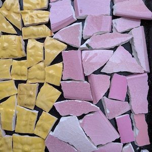 May include: A collection of broken ceramic tile pieces arranged in a mosaic pattern. The tiles are divided into two distinct color groups, featuring bright yellow pieces on the left side and various shades of pink pieces on the right side.