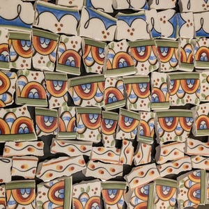 May include: A collection of broken ceramic tile pieces. The fragments feature a repeating pattern of orange, yellow, and blue arched designs with green and white accents. Some pieces have a blue and white border design.