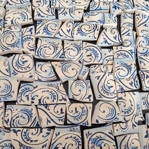May include: A collection of broken ceramic tiles with a white base and blue decorative patterns. The tiles feature swirling floral and geometric designs, creating a mosaic effect. The fragments vary in size and shape, offering a unique artistic texture.