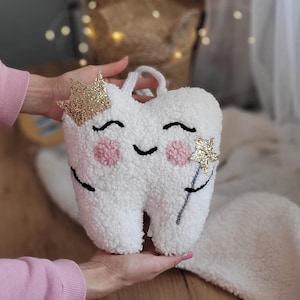 May include: A white plush tooth with a gold glitter crown and a gold glitter star on a wand. The tooth has a smiling face with pink cheeks.