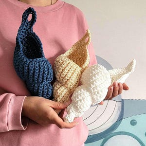 May include: Three crocheted seashell-shaped hanging baskets in blue, cream, and white. The baskets are made with a textured stitch and are perfect for adding a touch of whimsy to any room.