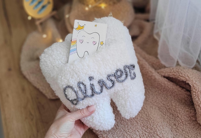 May include: White plush tooth-shaped box with a gray embroidered name "Aliser" on it. A small card with a cartoon tooth and a rainbow is tucked inside the box.
