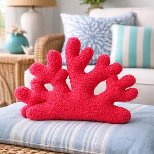 Pode incluir: Uma almofada decorativa cor-de-rosa choque em forma de coral. A almofada apresenta uma superfície texturizada e granulada, com uma silhueta orgânica ramificada que inclui múltiplas protuberâncias arredondadas que se elevam a partir de uma base sólida.