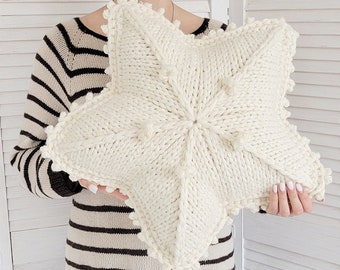 Puede incluir: Una almohada de estrella de punto blanco con una superficie texturizada y un ribete de pompón blanco.
