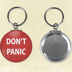 May include: A round red keychain with the words "DON'T PANIC" in white. The keychain has a silver metal ring and a silver metal back.