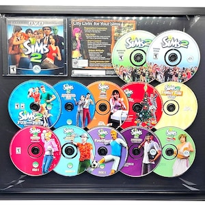 Peut inclure: Une collection de dix disques de jeu vidéo The Sims 2 dans leurs étuis. Les disques sont disposés en cercle avec le logo et le titre du jeu visible sur chacun. Les disques sont tous en excellent état et semblent neufs.