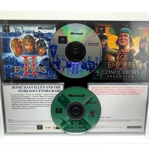May include: A framed set of Age of Empires II: The Age of Kings and Age of Empires II: The Conquerors Expansion video game discs. The set includes two game discs and two CD-ROMs. The frame is white with a black mat.