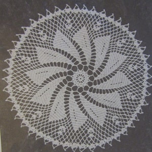 May include: White crocheted doily with a spiral design. The doily is made with delicate stitches and has a lacy appearance.