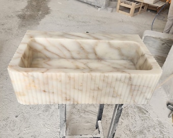 May include: A white marble sink with a rectangular shape and a ribbed exterior. The sink is sitting on a metal stand.