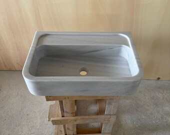 May include: A rectangular, gray marble sink with a built-in shelf. The sink has a single drain hole and is supported by a wooden pallet. The marble has subtle gray veining throughout.